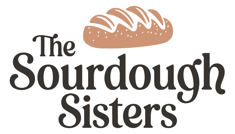 A logo or emblem for 'The Sourdough Sisters'. At the top, there's a stylized illustration of a loaf of sourdough bread with a drizzle of icing or glaze on top. Below the bread illustration, the text 'The Sourdough Sisters' is written in a decorative, cursive font. The entire design is set against a white background.