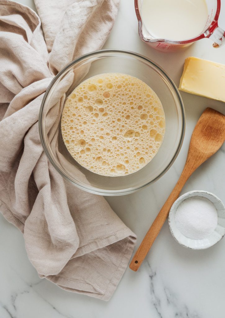 A flat lay of a beaten egg, a half cup of milk, a quarter cup of sugar, towels, and a wooden spoon