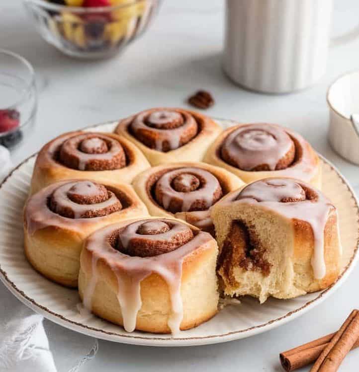 A plate of freshly baked cinnamon rolls, one of which is half bitten