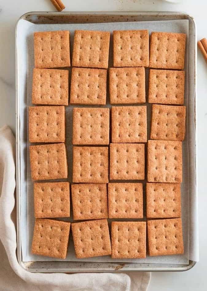 Freshly baked sourdough graham crackers on a parchment-lined baking sheet, sprinkled with a dusting of cinnamon sugar